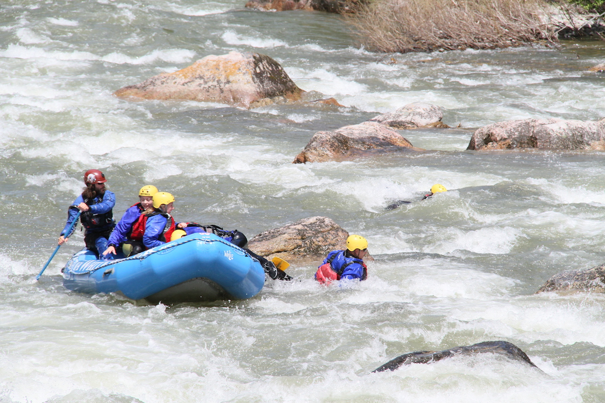 group rafting with people swimming through a rapid